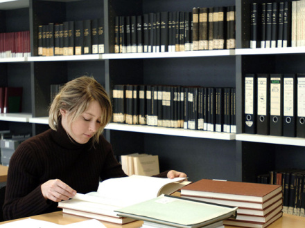 Das Bild zeigt eine Frau im Lese·saal vom Stadtarchiv Nürnberg. Die Frau blättert in einem Buch.