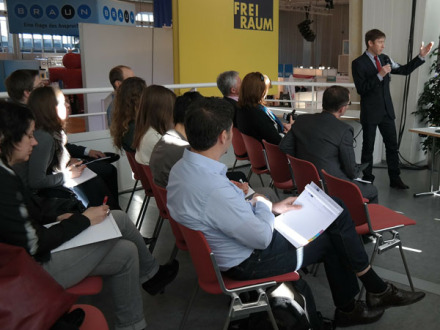 Foto von einem Vortrag. Vorne steht ein Mann mit einem Mikrophon in der Hand. Auf Stühlen sitzen die Zuhörer., Bild © pixabay.com