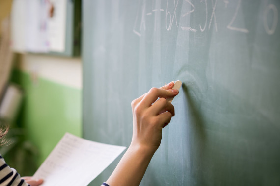 Junge Lehrkraft schreibt eine mathematische Formel an eine Tafel in einem Klassenzimmer.