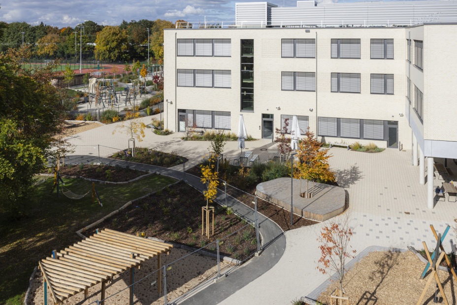 Schulhof des Schulcampus Werderau in der Maiacher Straße im Oktober 2025 mit Spielelementen im Vordergrund und Sportplatz im Hintergrund., Bild © Giulia Iannicelli