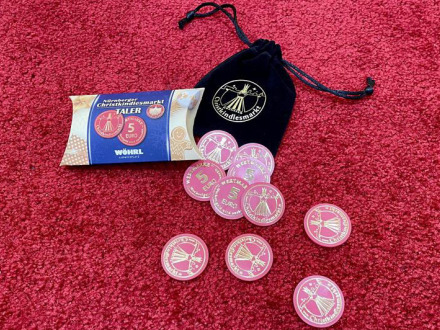 Foto von den Christ·kindles·markt-Talern. Daneben liegen ein schwarzes Säckchen und ein kleiner Karton für die Verpackung von den Christ·kindles·markt-Talern.