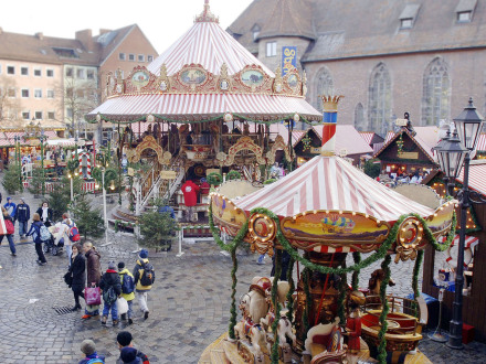 Foto von der Nürnberger Kinder·weihnacht bei Tag. Im Bild vorne ist ein kleines Karussell. In der Mitte vom Bild steht ein großes Karussell. Um den Platz herum stehen verschiedene Buden., Bild © Ohne Bildnachweis