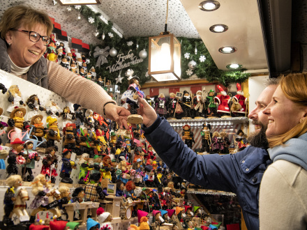 Foto von einem Stand auf dem Nürnberger Christ·kindles·markt. Eine Händlerin gibt Gästen einen Zwetschgen·männle.