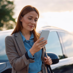 Smiling woman texting on mobile phone after driving a car.