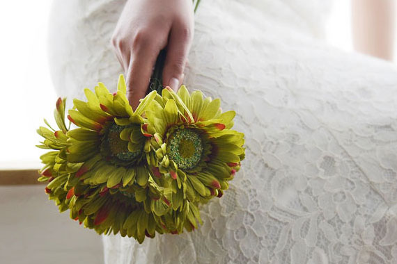Eine Hand hält einen Blumenstrauß vor einem Brautkleid