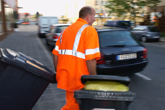 Ein Mann in Arbeitskleidung der Müllabfuhr zieht zwei Mülltonnen