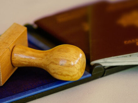 Foto von einem Stempel auf einem Stempel·kissen. Daneben liegen 2 Reise·pässe.