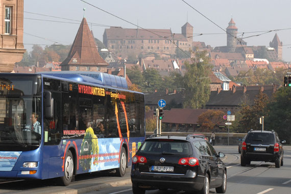 Mehrere Autos und ein Bus fahren auf einer Straße, im Hintergrund die Kaiserburg
