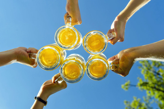 Anstoßen mit Bierkrügen vor blauem Himmel