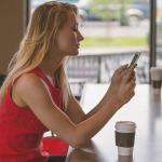 Frau sitzt in einem Cafe und blickt auf das Handy in ihren Händen.