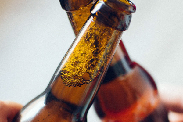 Zwei Menschen stoßen mit Bierflaschen an.