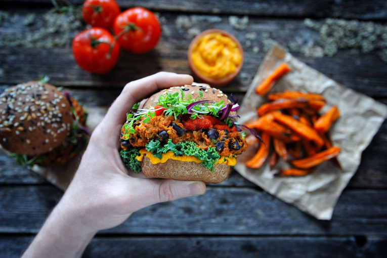 Eine Hand hält einen veganen Süßkartoffel-Bohnen-Burger.