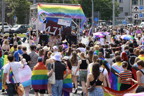 Christopher Street Day Demonstration in Nürnberg 2024: Teilnehmer in bunter Kleidung, teilweise mit Umhängen und Regenschirmen in Regenbogenfarben, laufen an am Vorplatz des Nürnberger Hauptbahnhofs vorbei.
