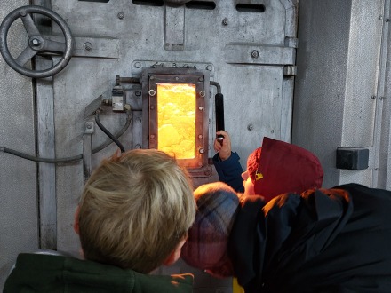 Foto: Besucher schauen durch eine Luke in das Feuer von der Müll·verbrennungs·anlage., Bild © Nina Gindele