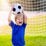Ein lachender Junge mit einem Fußball auf einem Fußballfeld.