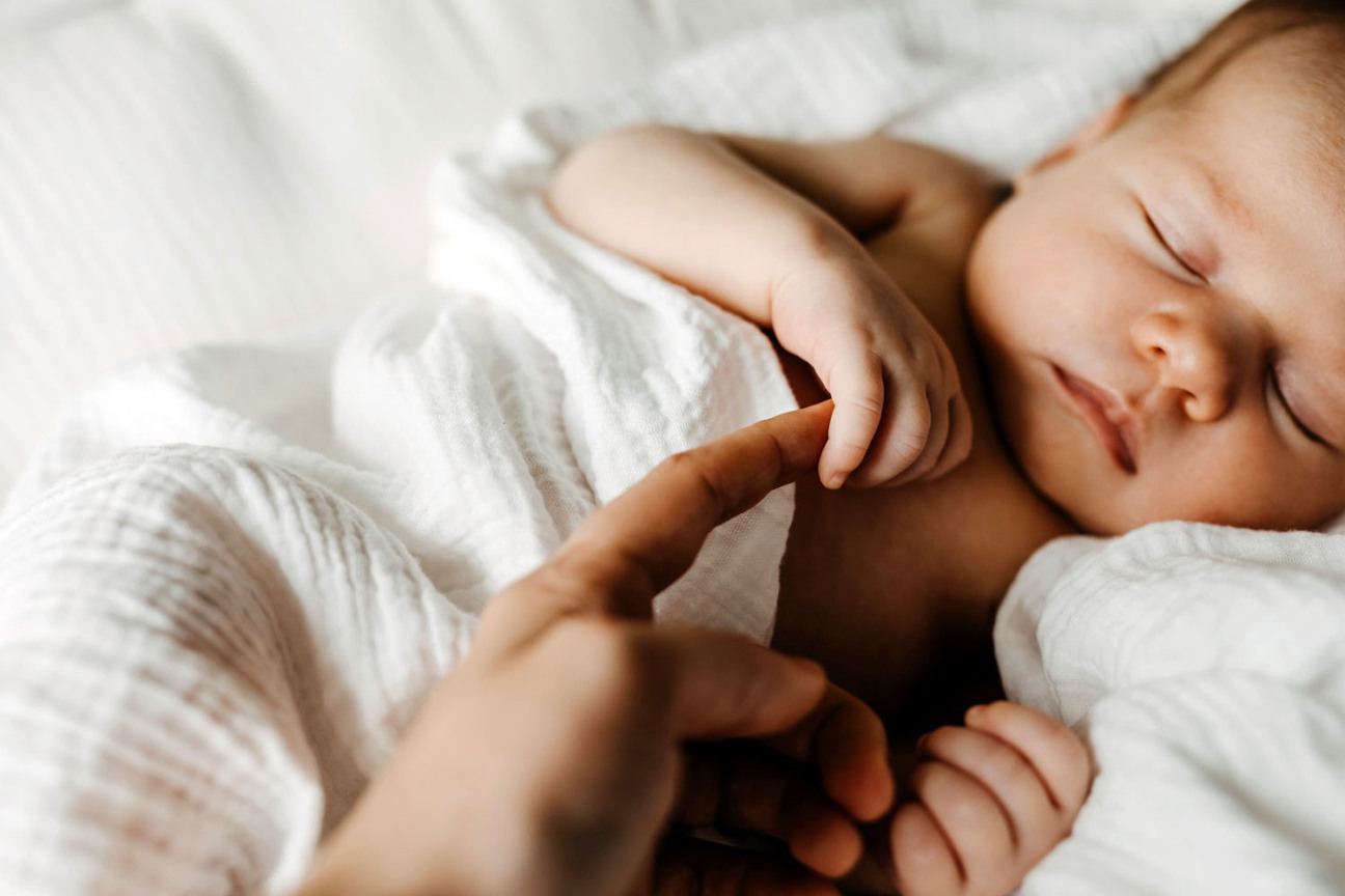 Schlafendes Baby, eine Frauenhand hält eines der Händchen., Bild © Natalia Bostan / Adobestock