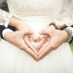 Ein Brautpaar hält sich an den Händen, die zusammen ein Herz formen.