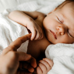 Schlafendes Baby, eine Frauenhand hält eines der Händchen.