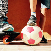 Zwei Kinder mit einem Skateboard und einem Fußball.
