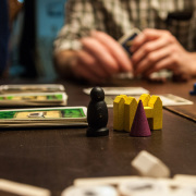 Brettspielfiguren mit Spielgeld, Hände im Hintergrund