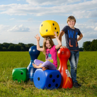 Junge und Mädchen mit großen Spielsteinen und Würfeln auf einer Wiese