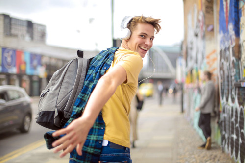 Ein Jugendlicher mit Rucksack und Kopfhörer auf einer Straße in der Stadt.