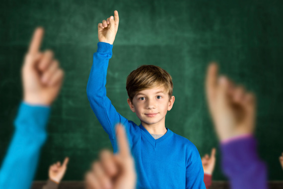 Ein Junge steht vor einer Schultafel und meldet sich.
