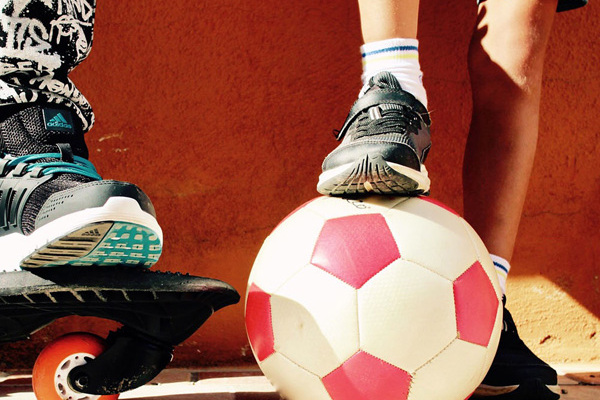 Zwei Kinder mit einem Skateboard und einem Fußball.