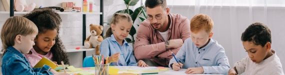 teacher and interracial preschoolers at table with paints and papers in classroom
