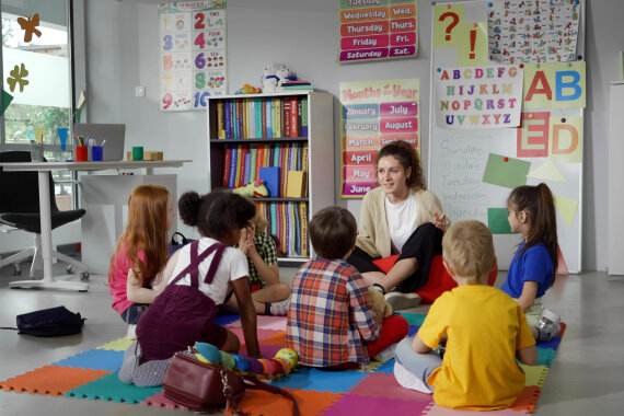 Kinder sitzen vor Lehrerin in der Vorschule und hören gespannt zu was Sie erzählt.