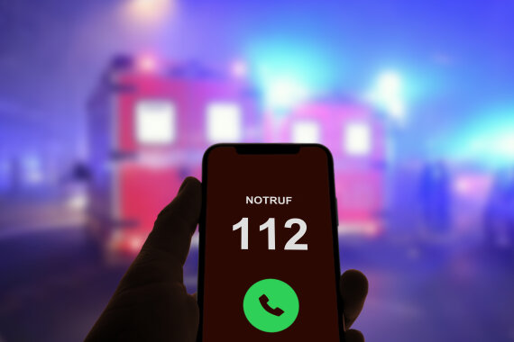 Foto: Eine Hand hält ein Handy. Auf dem Bildschirm steht: Notruf 112.