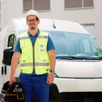 Ein Handwerker auf dem Weg zu seiner Arbeit in einem städtischen Wohngebiet. Im Hintergrund parkt sein Van.