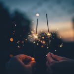 Zwei Hände halten in der Dämmerung brennende Wunderkerzen.