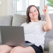 Frau mit Downsyndrom arbeitet am Laptop und zeigt das "OK"-Zeichen