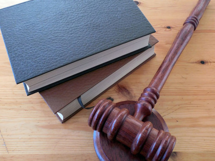 Foto von einem Hammer von einem Richter beim Gericht. Daneben liegen 2 Gesetz·bücher.