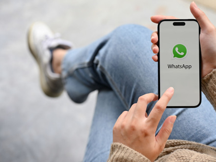 Foto von einer jungen Frau mit einem Handy. Die junge Frau schaut auf das Display vom Handy. Darauf ist das WhatsApp-Logo., Bild © Bongkarn / AdobeStock