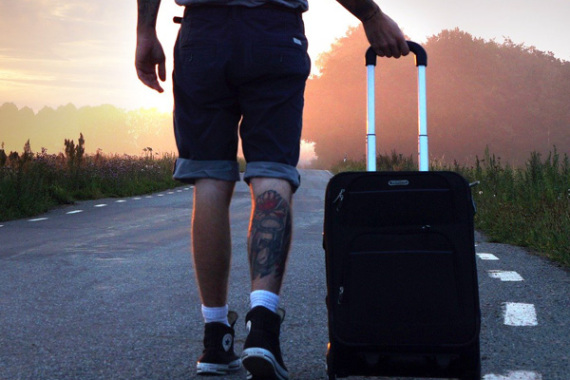 Reisender mit einem Koffer auf einer einsamen Landstraße.