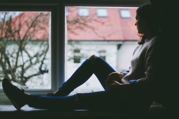 Eine Frau sitzt allein an einem Fenster und sieht hinaus.