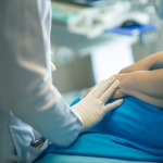 Eine Ärztin legt in einem Krankenhaus ihre Hand tröstend auf die Hand einer Patientin.