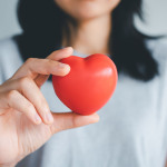 Die Hand einer Frau hält ein Herz in die Kamera.