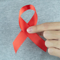 Eine Hand hält eine rote Aids-Schleife in die Kamera.