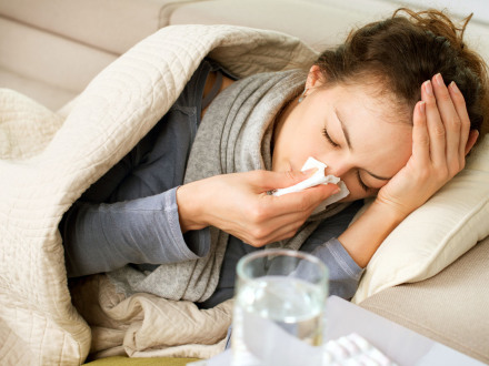Eine junge Frau liegt mit einer Erkältung auf dem Sofa.