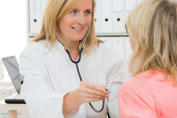 Eine Hausärztin hört eine Patientin mit Stethoskop ab.