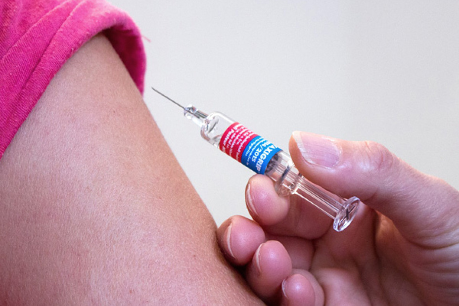 Hand mit Spritze am Oberarm eines Patienten.