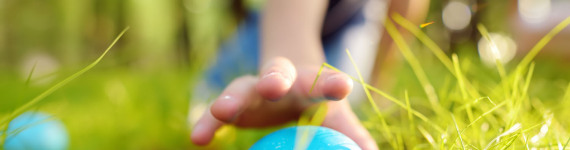 Ein kleiner Junge findet ein blau gefärbtes Osterei in der Wiese.