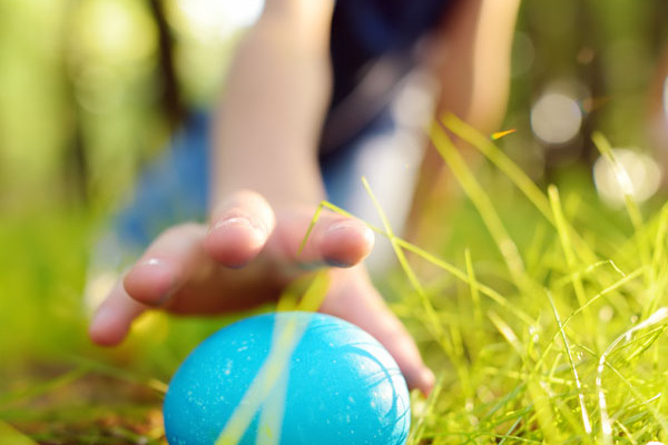 Ein kleiner Junge findet ein in der Wiese verstecktes blaues Osterei.