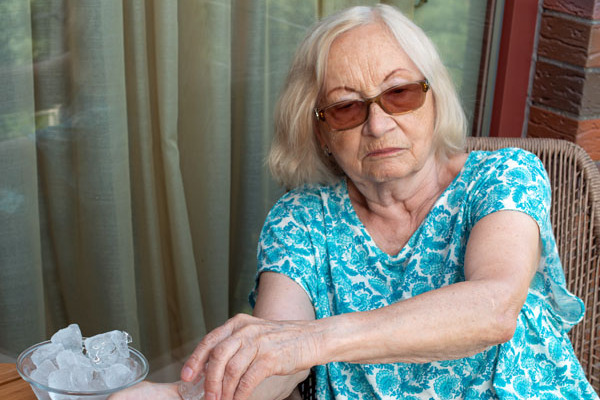 Eine Seniorin kühlt ihre Unterarme mit Eiswürfeln.