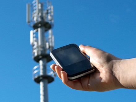 Bild © manuel faba / AdobeStock Foto: Eine Person hält ein Handy in der Hand. Im Hintergrund ist eine Mobil·funk·antenne., Bild © manuel faba / AdobeStock