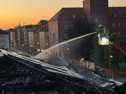 Bild © Feuerwehr Nürnberg Foto von einem Feuerwehr·mann auf einer Leiter. Der Feuerwehr·mann löscht den Brand im Dach von der Turn·halle von der Grund·schule Wiesen·straße., Bild © Feuerwehr Nürnberg