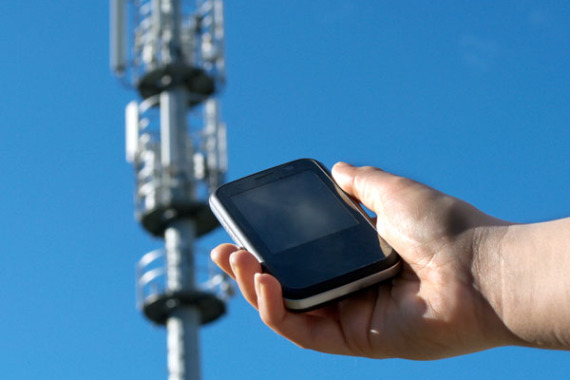 Foto: Ein Mann hält ein Handy in die Richtung von einer Mobil·funk·antenne.